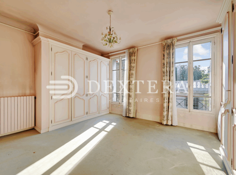 Hôtel Particulier à Neuilly-sur-Seine : Chambre lumineuse avec placards intégrés, moquette claire et vue arborée.