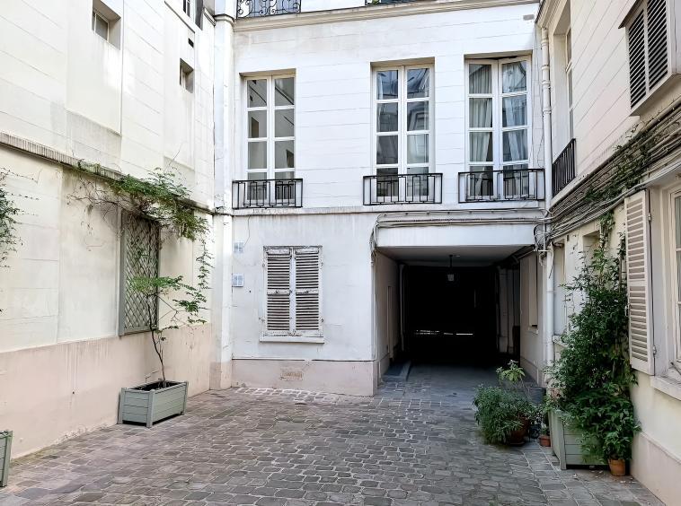 Cour intérieure pavée d'un immeuble ancien rue du Bac à Paris 7e, avec façades claires et plantations.